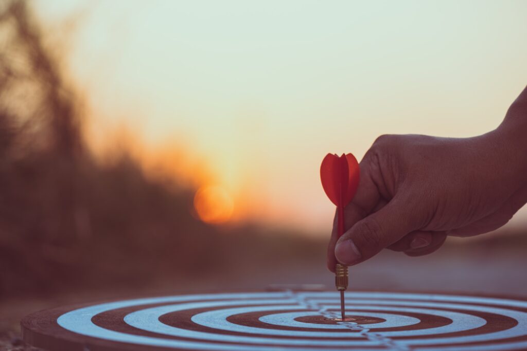 Close up hand hitting red arrow to target dartboard at sunset background. Business targeting