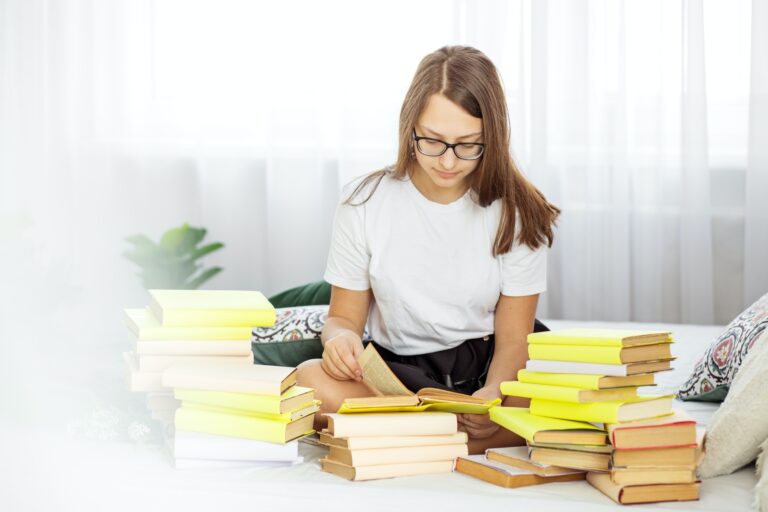 Teen girl prepares for exams with glasses. A lot of textbooks. Concept of education, hobby and study