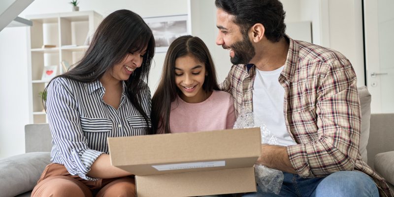 Happy indian family with teen daughter unpacking parcel at home.